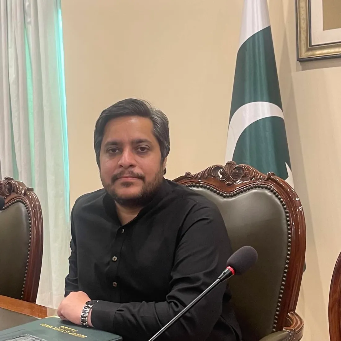 Taimoor Bamazai seated at a desk in front of a Pakistan flag, Islamabad, March 2024