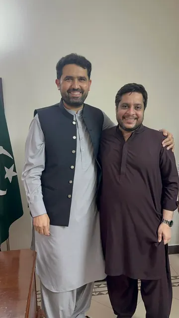 Taimoor Bamazai standing beside the Chief Minister of Khyber Pakhtunkhwa in front of a Pakistan flag
