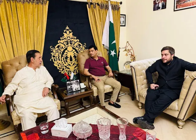 Taimoor Bamazai seated with the Governor of Gilgit-Baltistan in a reception room with Pakistan flags