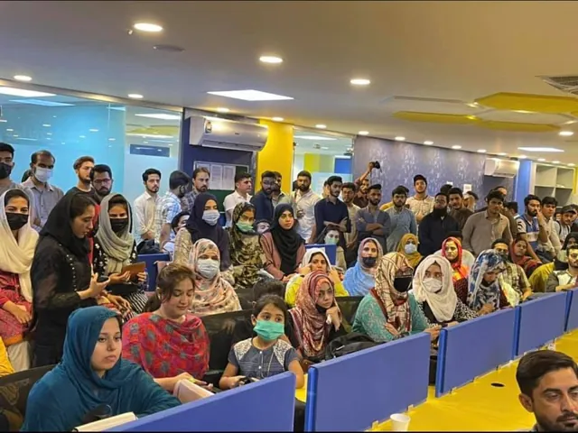 A crowded incubator floor with attendees seated at desks