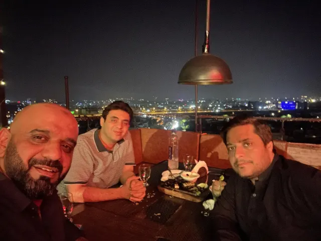 Taimoor Bamazai at a rooftop dinner table at night with two friends